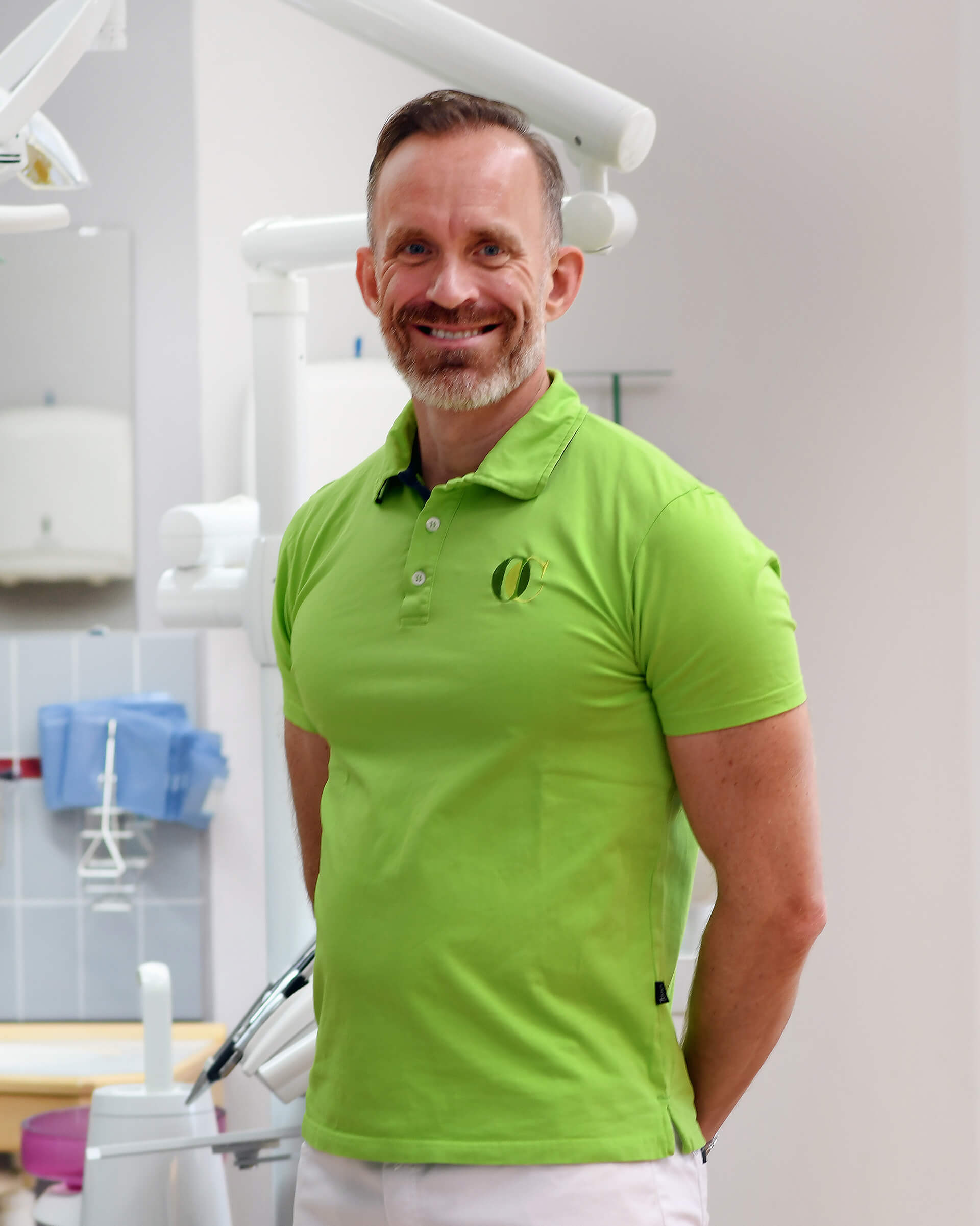 Gustaf Wiklund står i ett behandlingsrum, han har en grön tröja på sig med Oral Cares logotyp och händerna bakom ryggen. Han ler mot kameran.
